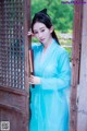 A woman in a blue dress leaning against a wooden door.