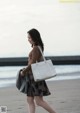 A woman walking on the beach carrying a white bag.