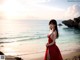 A woman in a red dress standing on a beach.