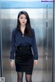 A woman in a blue shirt and black skirt standing in an elevator.