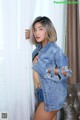 A woman in a denim jacket leaning against a curtain.