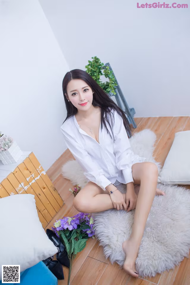 A woman sitting on a white rug with a bouquet of flowers.