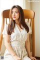 A woman sitting on a wooden chair wearing a white shirt and floral skirt.