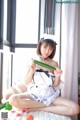 A woman in a maid outfit holding a cucumber.