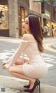 A woman in a white dress crouching down on the street.