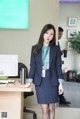 A woman in a business suit standing in front of a computer.