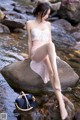 A woman sitting on a rock in the water.