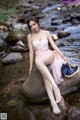 A woman sitting on a rock in the water.