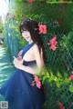 A woman in a blue dress posing in front of a fence.