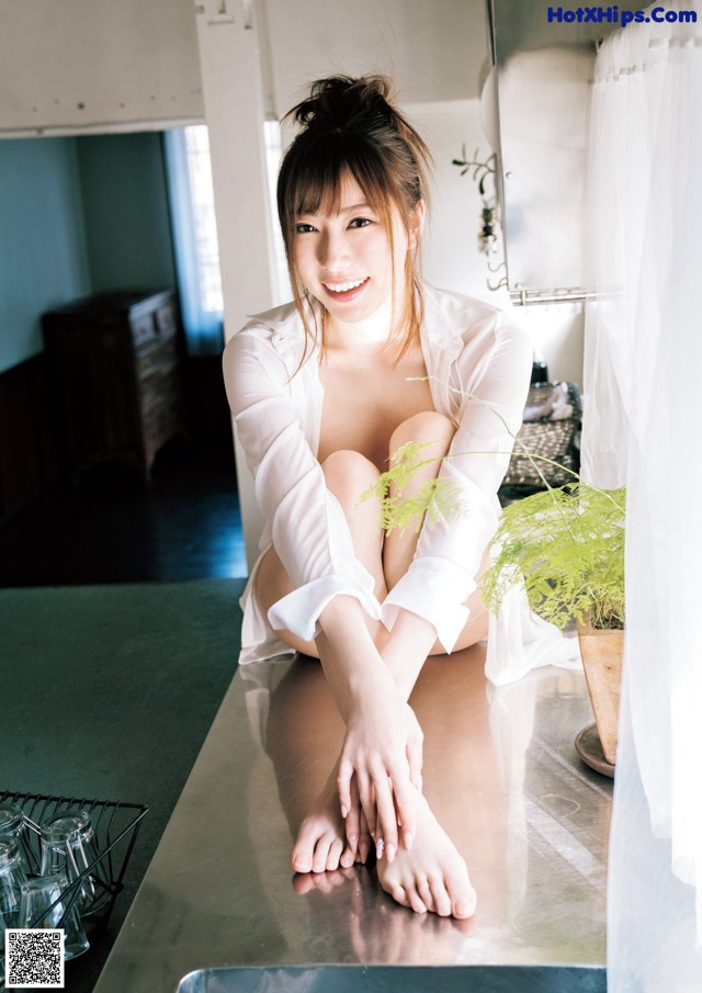 A woman sitting on top of a kitchen counter next to a plant.