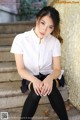 A woman in a white shirt and black skirt sitting on some steps.