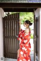 A woman in a red kimono standing in front of a wooden door.