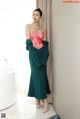 A woman standing in front of a bathtub wearing a green dress.