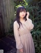 A woman in a beige dress standing in a garden.